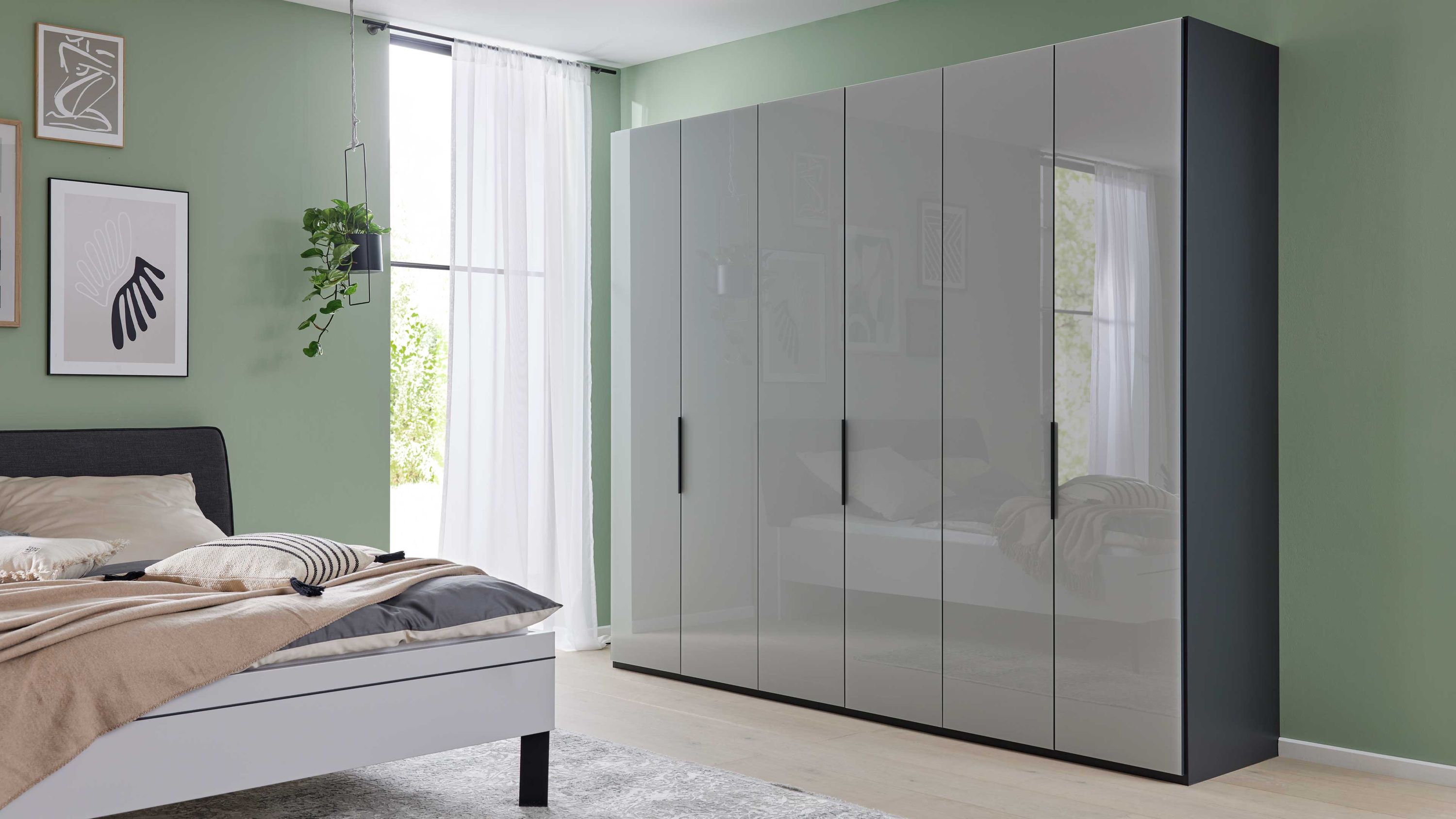 Sechstüriger Kleiderschrank mit glänzenden grauen Türen und schwarzen Griffen in grün gestrichenem Schlafzimmer