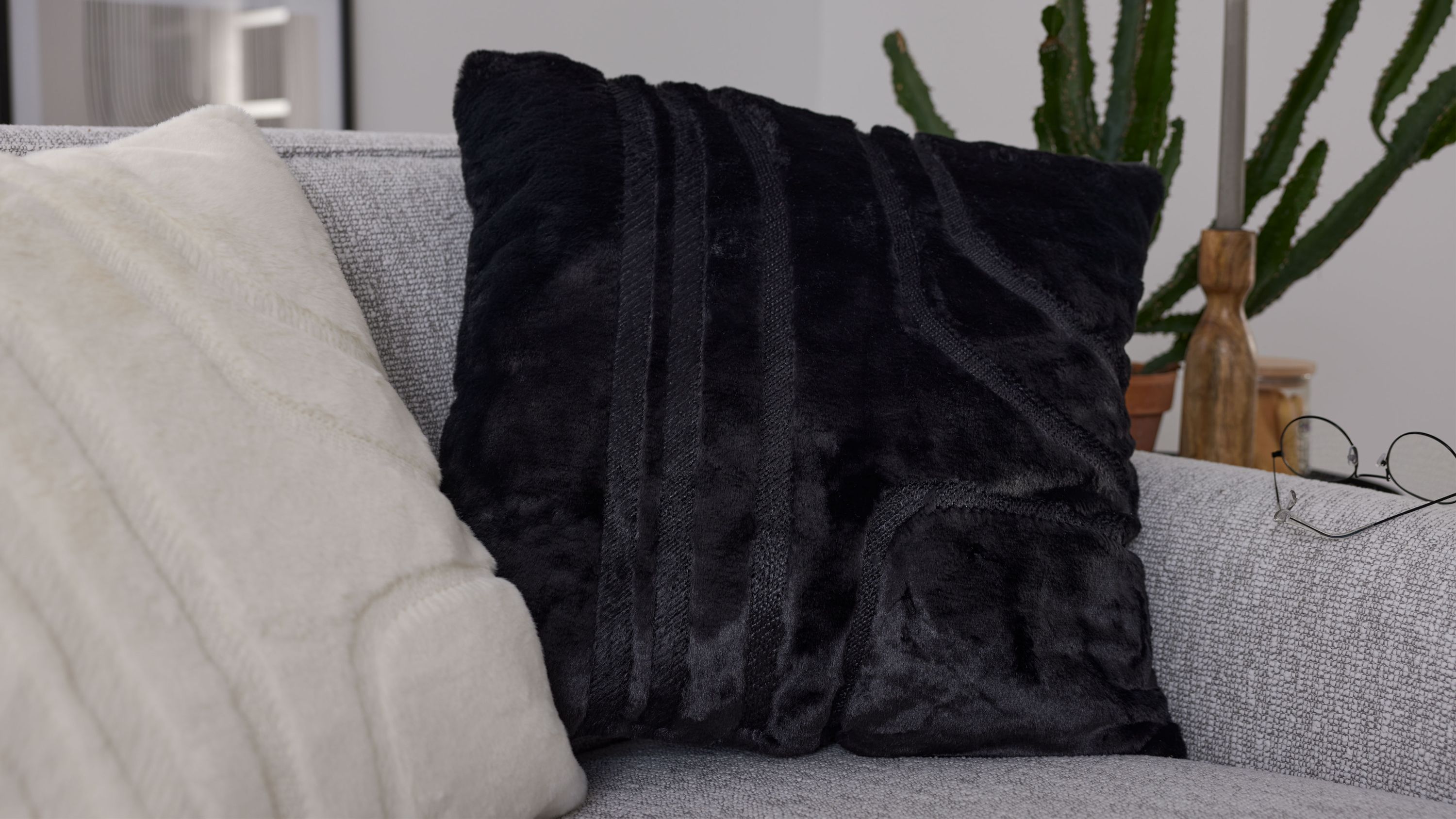 Quadratisches Kissen mit schwarzer strukturierter Kunstfellhülle auf grauem Sofa