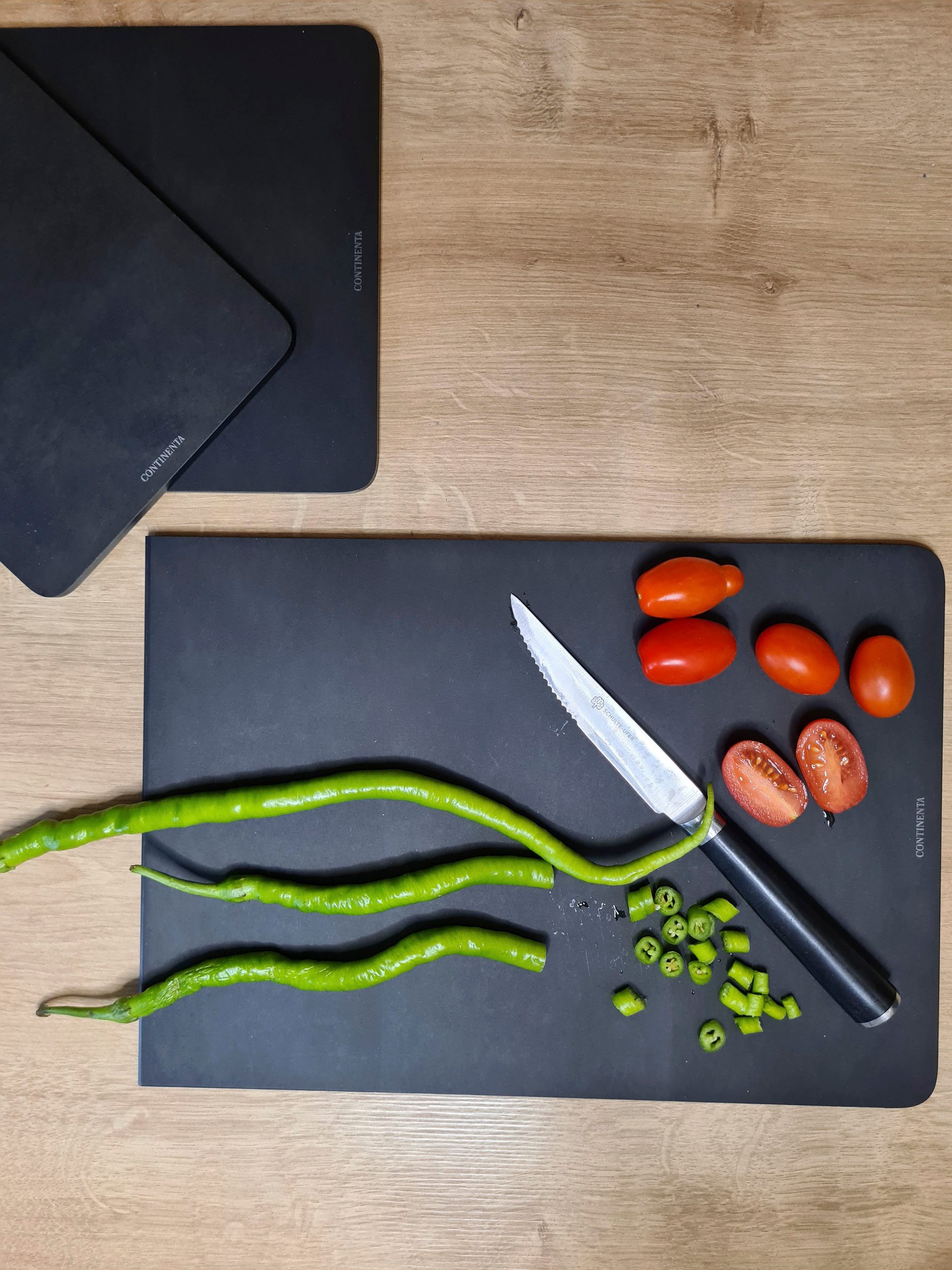 Schwarzes Schneidebrett mit geschnittenen Bohnen  Tomaten und Messer auf heller Holzarbeitsplatte