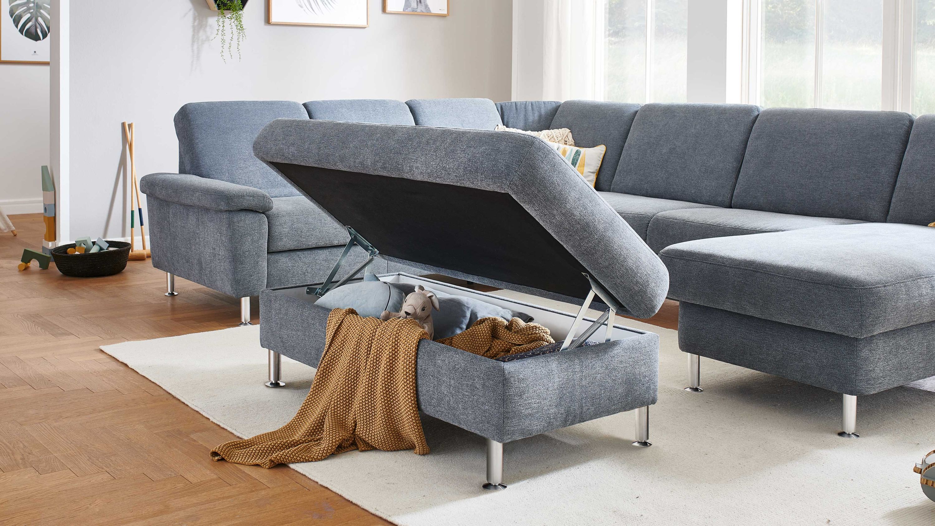 Großes graues Sofa mit offenem Stauraum im Sitz und silbernen Füßen auf hellem Teppich