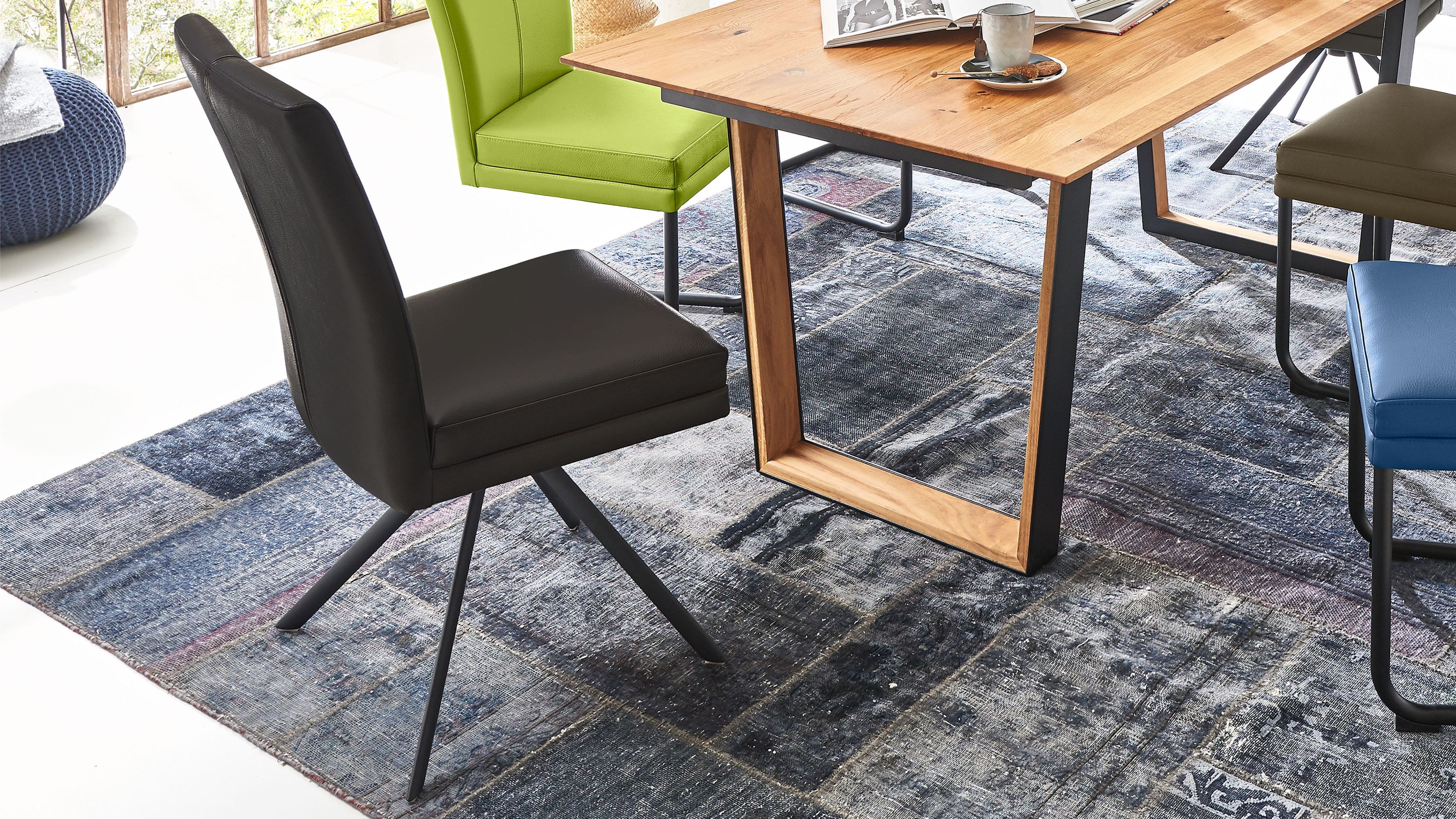 Polsterstuhl mit schiefergrauem Bezug und schwarzem Metallgestell neben Holztisch auf blauem Teppich
