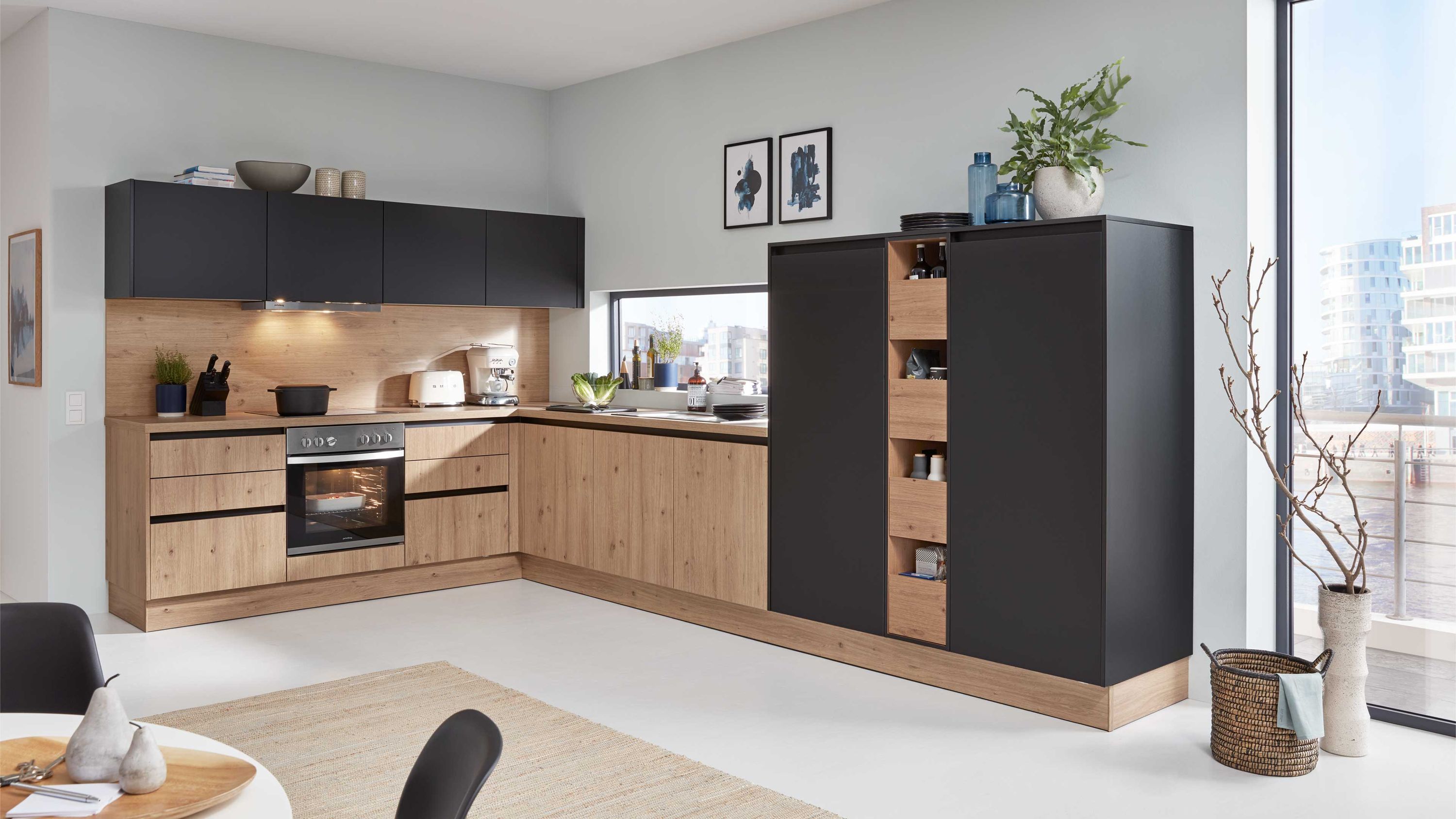 L-Küche in Holzoptik mit schwarzen Fronten. L-Küche in Holzoptik mit schwarzen Fronten offenen Regalfächern Einbauofen und großem Fenster.