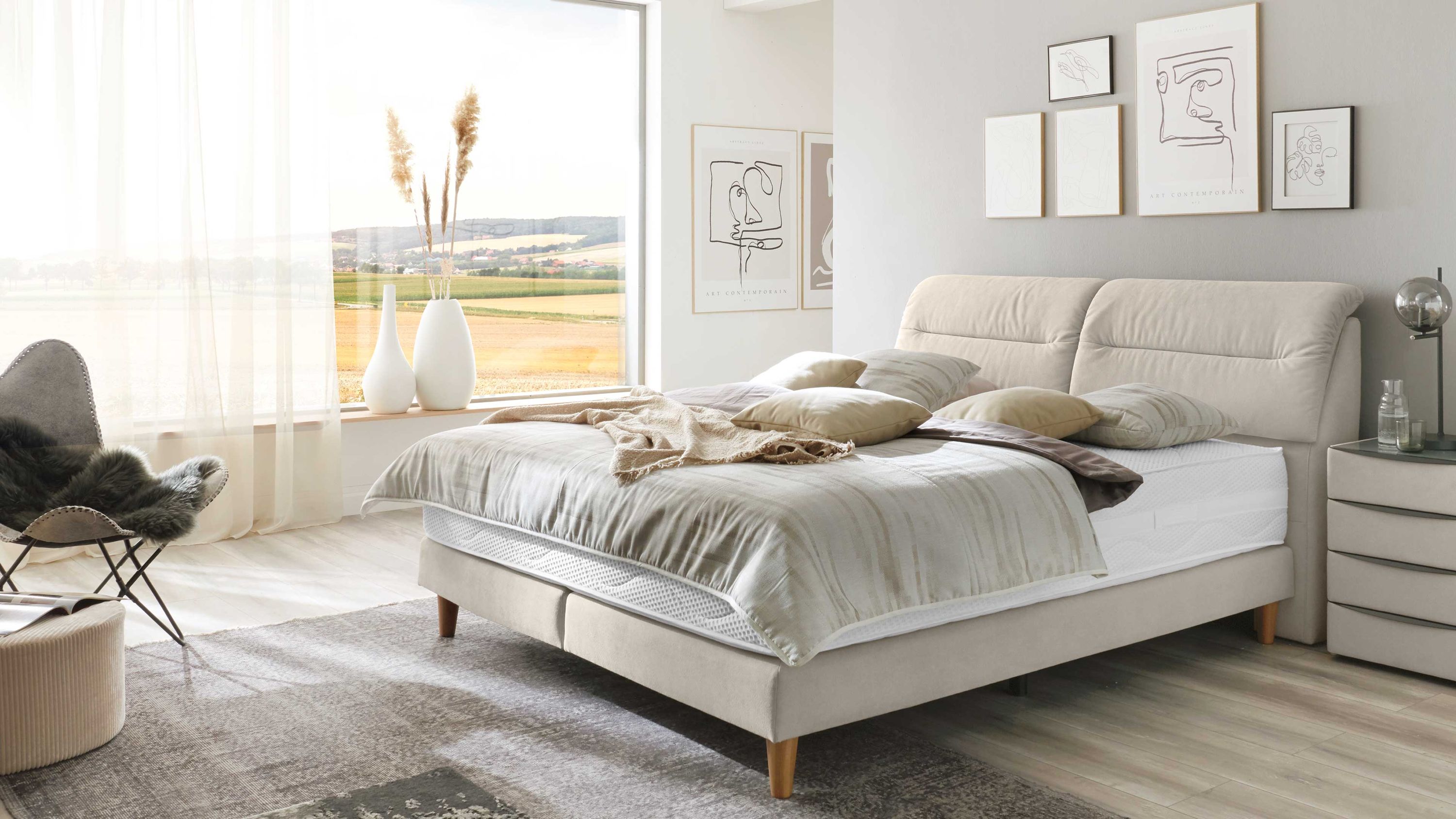 Boxspringbett mit gepolstertem Kopfteil und naturfarbener Mikrofaser in einem hellen Schlafzimmer