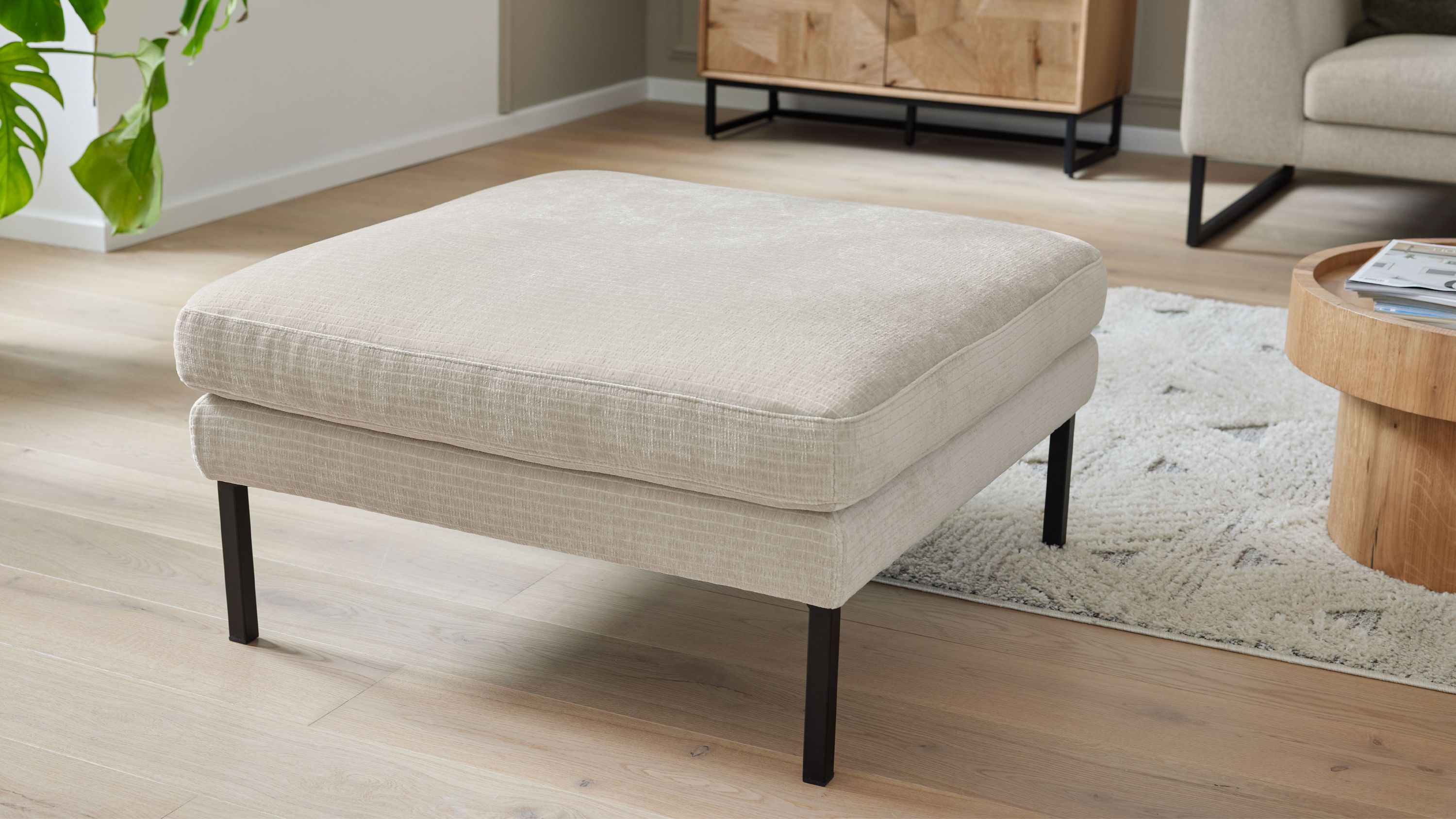 Quadratischer Polsterhocker mit naturfarbenem Bezug und schwarzen Metallfüßen in modernem Wohnzimmer