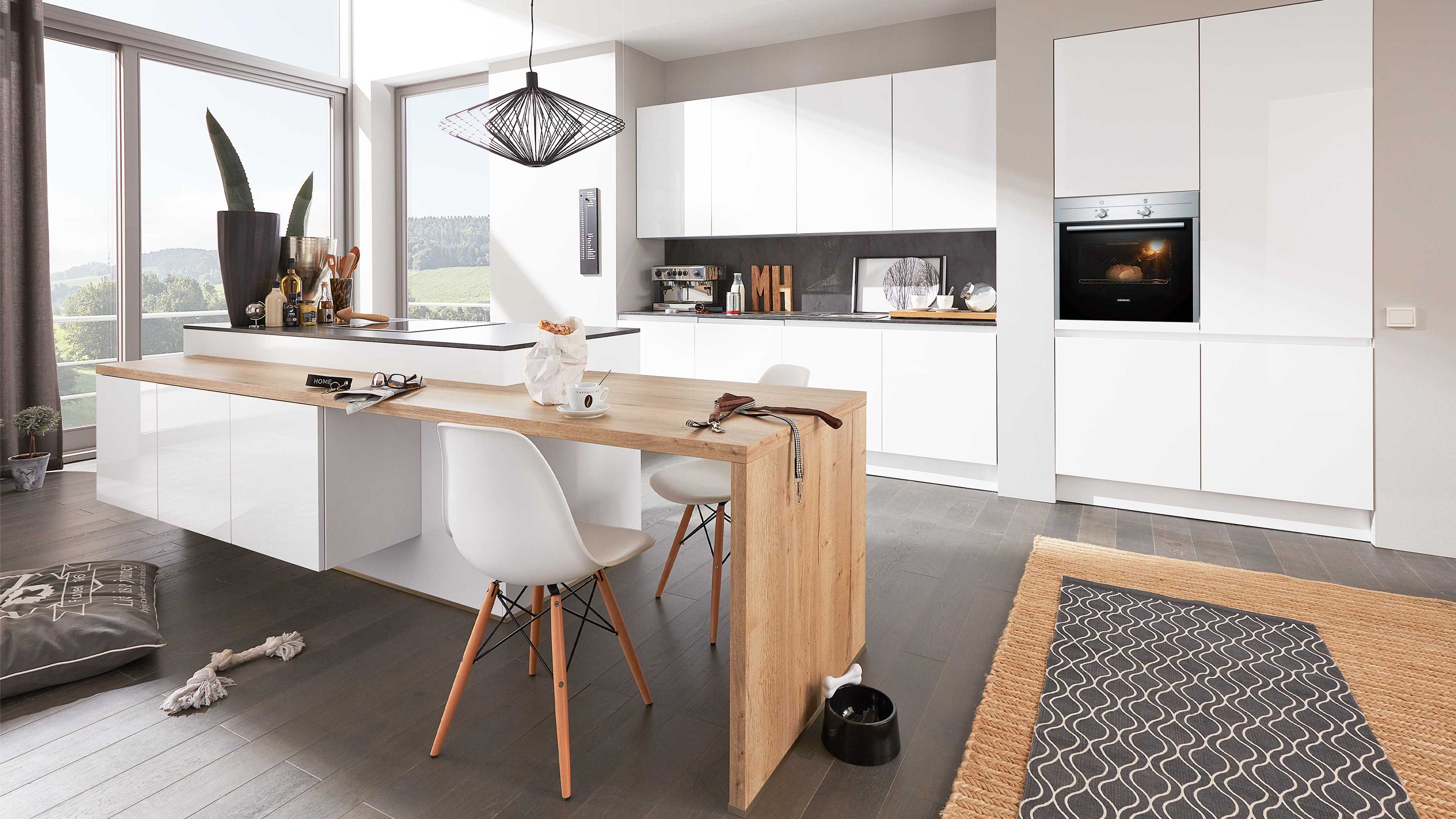 Küche mit weißen Schränken Einbauofen Holztisch weißen Stühlen Fensterlicht und Teppich auf Holzboden
