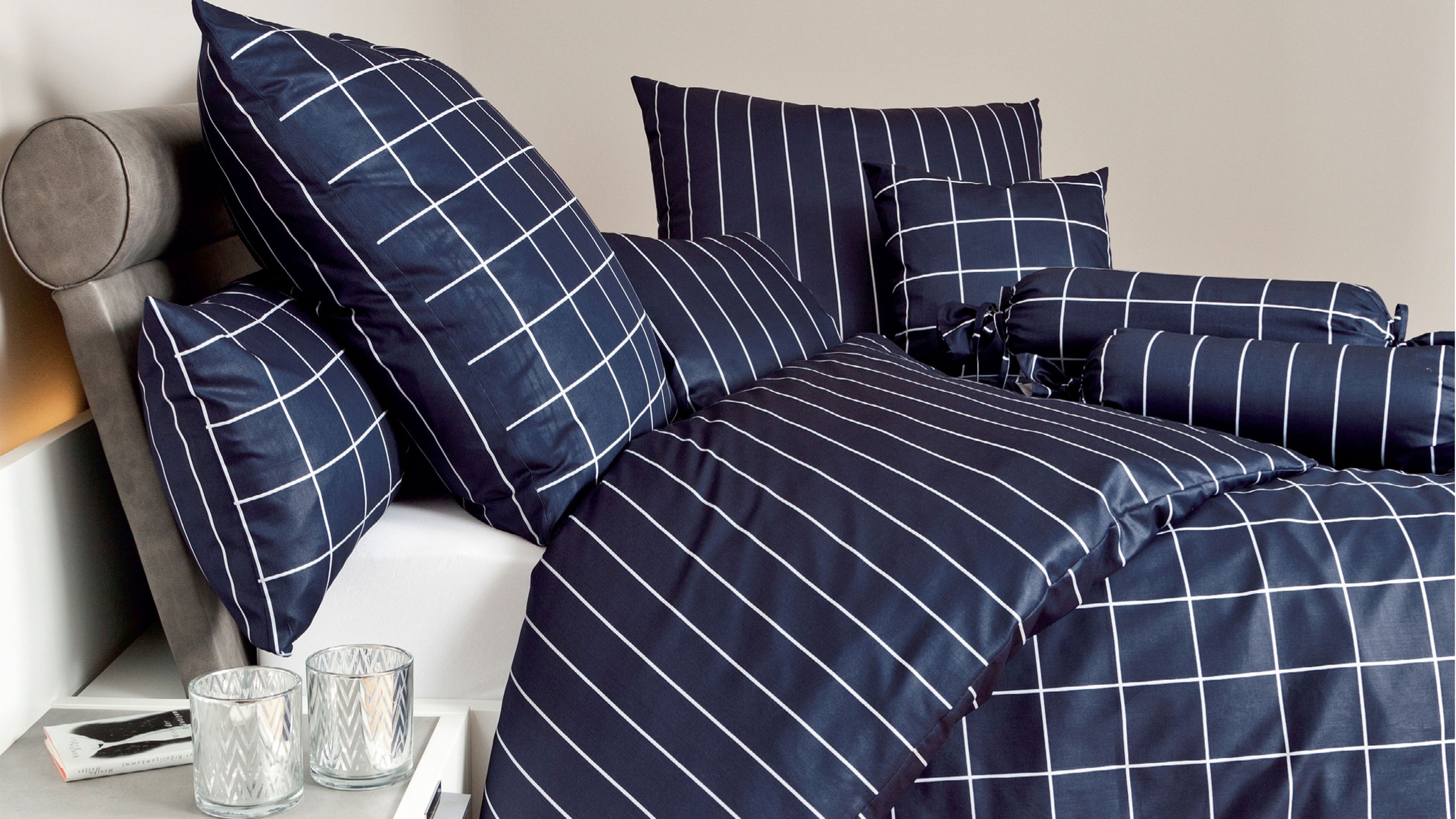 Dunkelblaue Bettwäsche und Kissenbezüge mit weißen Linien in verschiedenen Mustern auf einem Bett