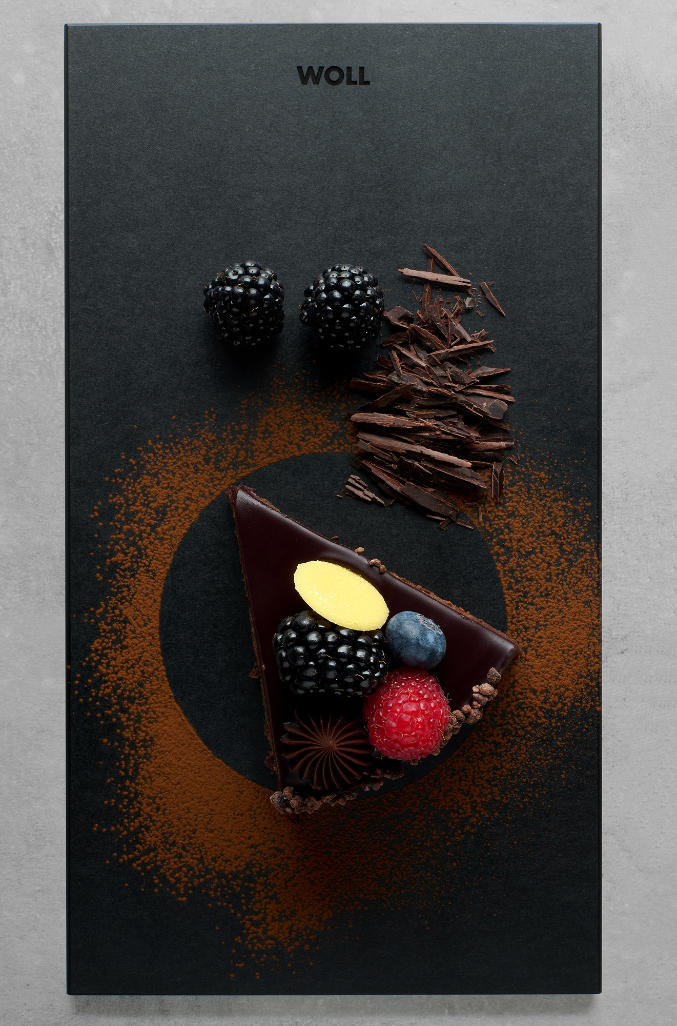 Schwarzes Schneidebrett mit Beeren und einem Stück Schokoladenkuchen mit Toppings belegt, Draufsicht