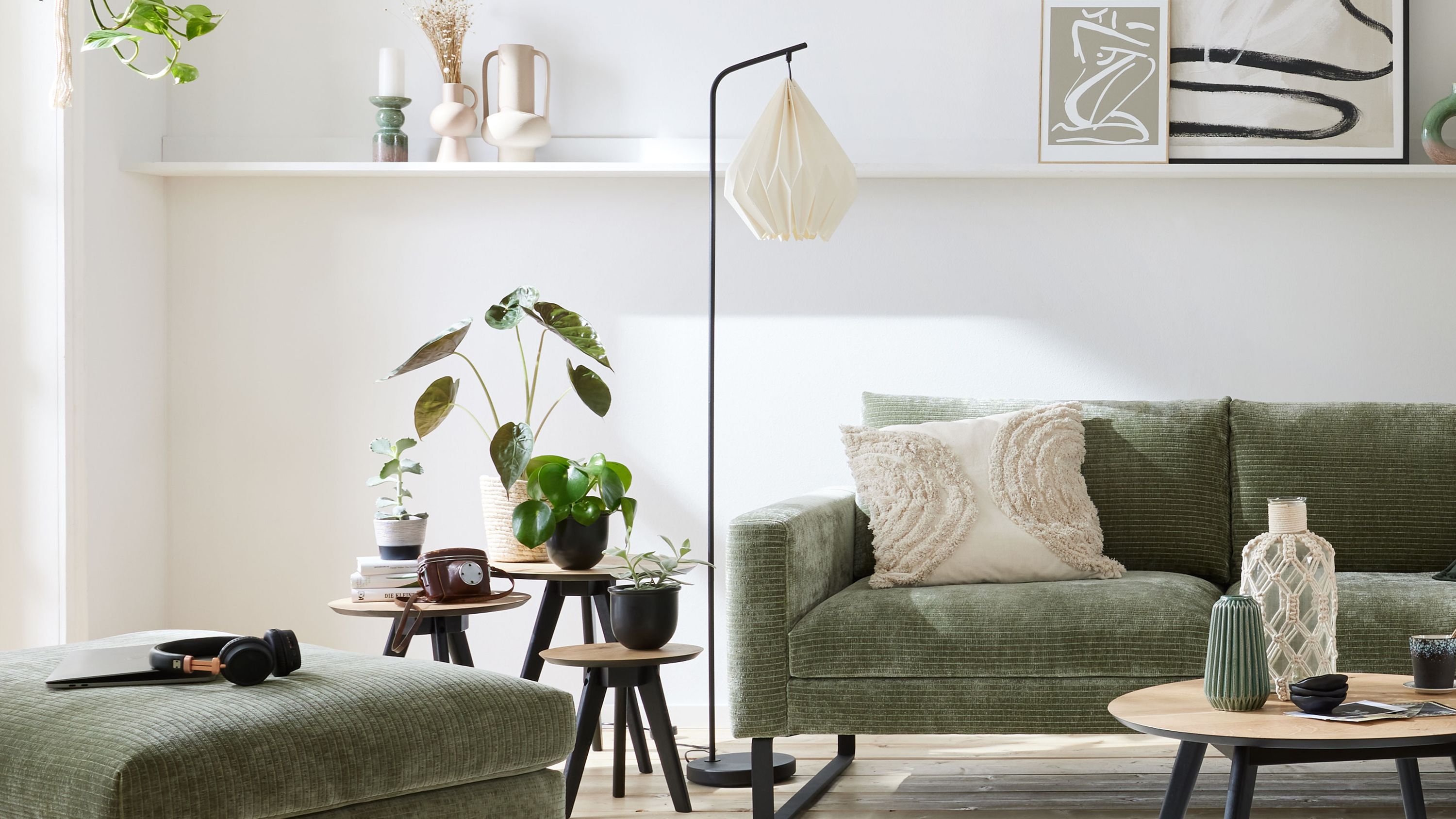 Stehlampe mit weißem Papierlampenschirm und schwarzem Metallgestell Stehlampe mit schwarzem Metallgestell und weißem Lampenschirm aus Papier neben grünem Sofa mit Kissen