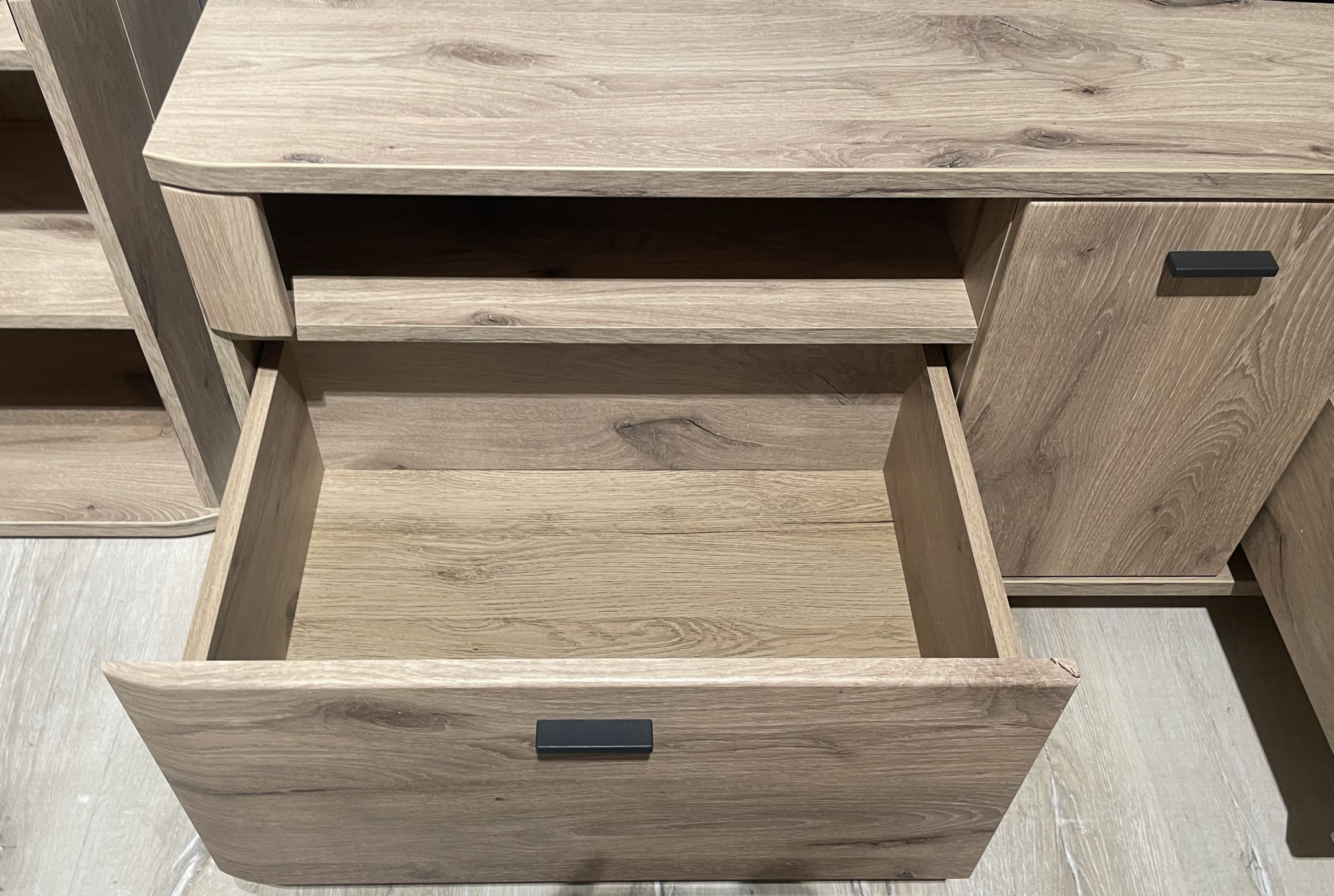 Offene Schublade und Tür eines hellen Holzmöbels mit schwarzem Griff
