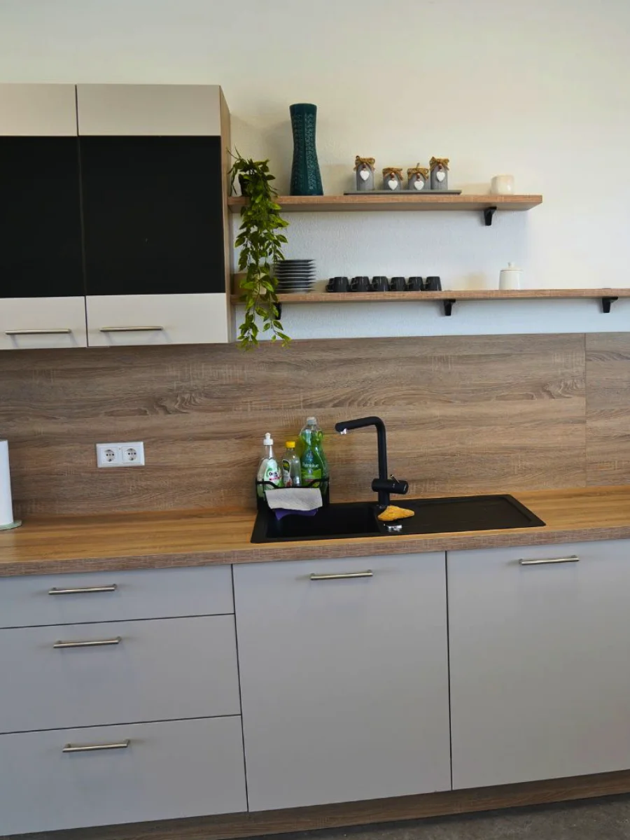 Moderne Küchenzeile mit grauen Fronten, Holzarbeitsplatte, schwarzer Spüle, Einbaugeräten, offenen Regalen und Kaffeemaschine.