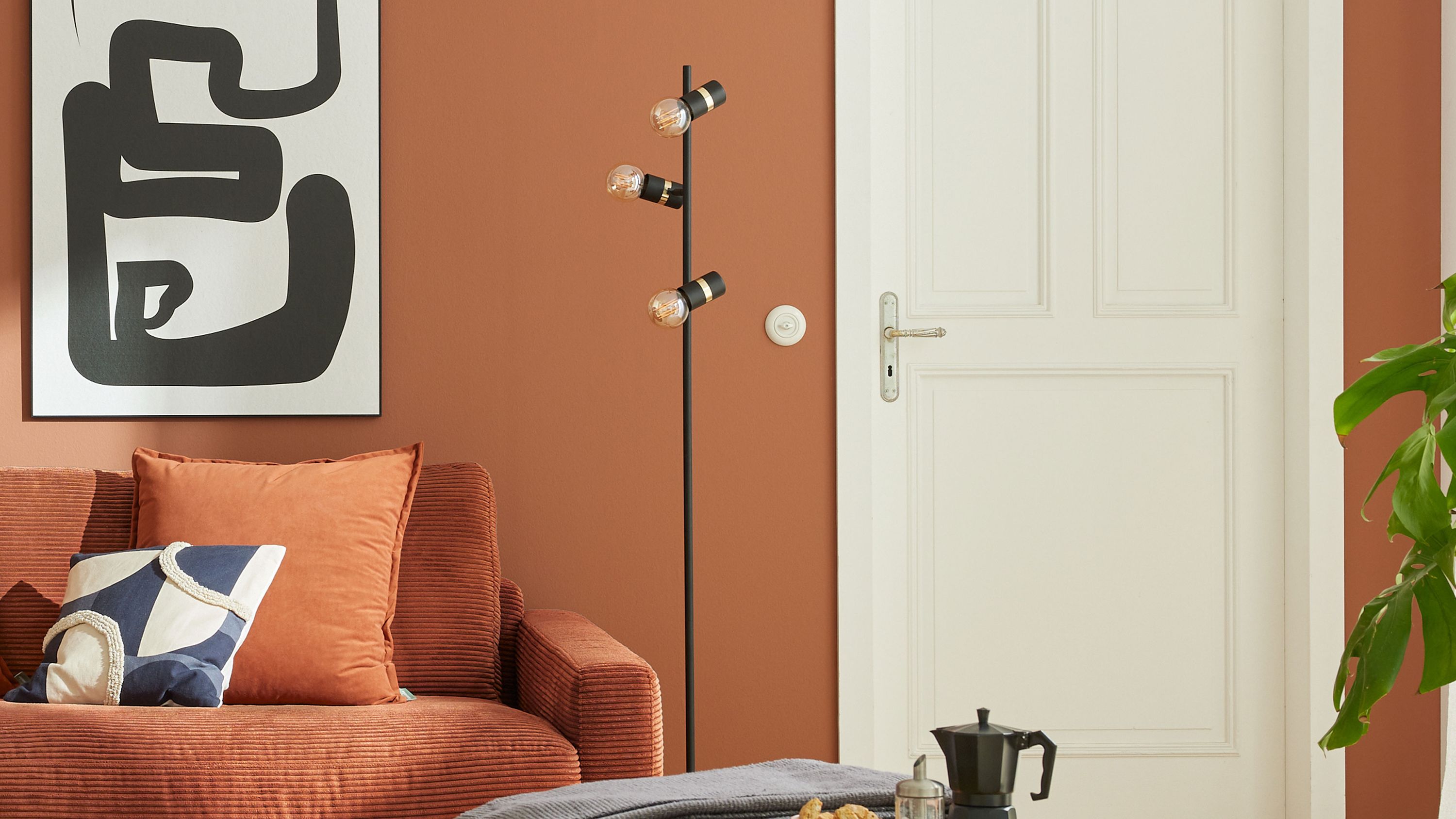 Schwarze Stehlampe mit drei Lampenschirmen im Wohnzimmer Schwarze Stehlampe mit drei Lampenschirmen an einem Stab in einem Wohnzimmer mit braunem Sofa und weißer Tür