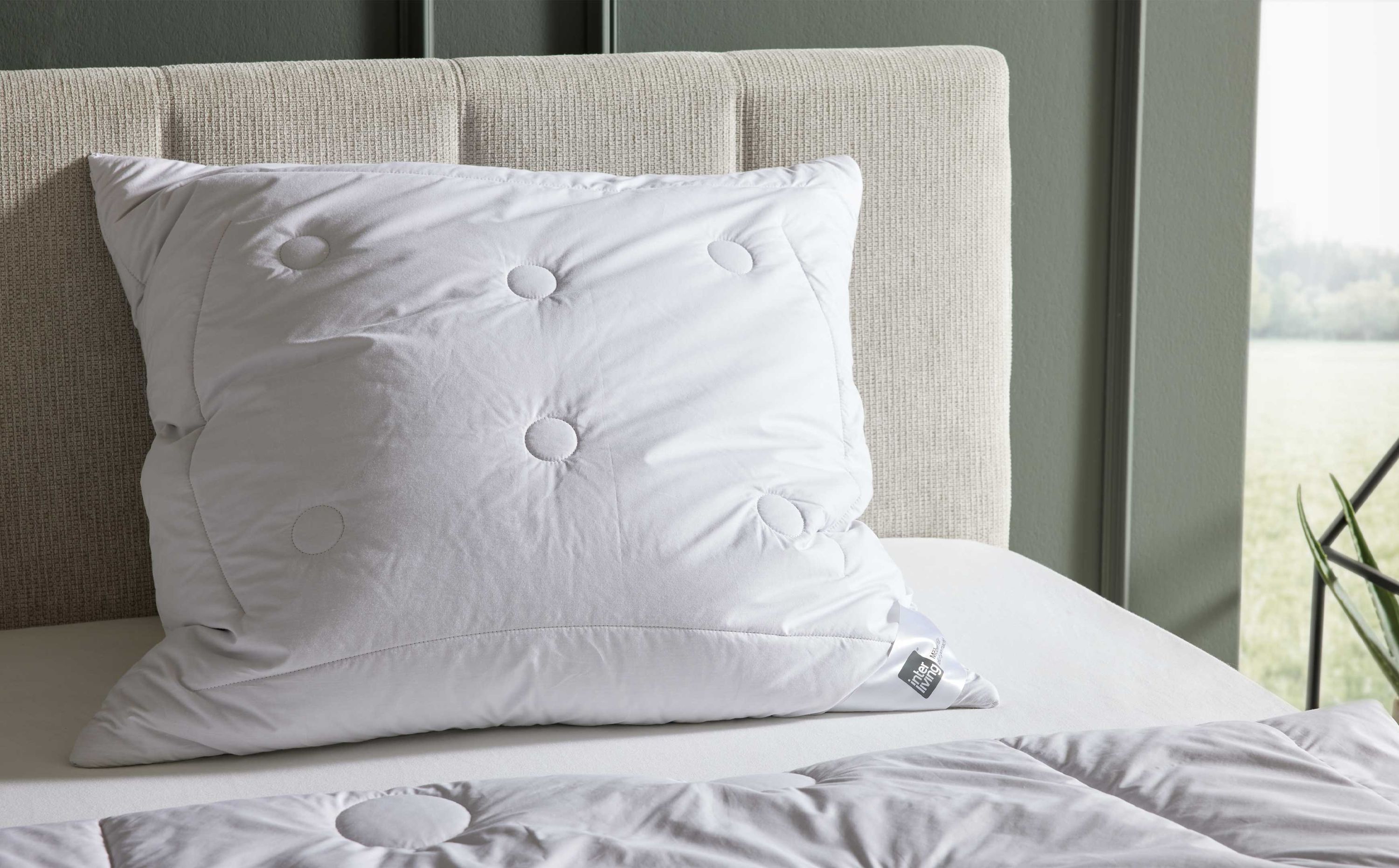 Weißes Kopfkissen mit gesteppten Kreisen auf einem hellen Bett mit gepolstertem Kopfteil