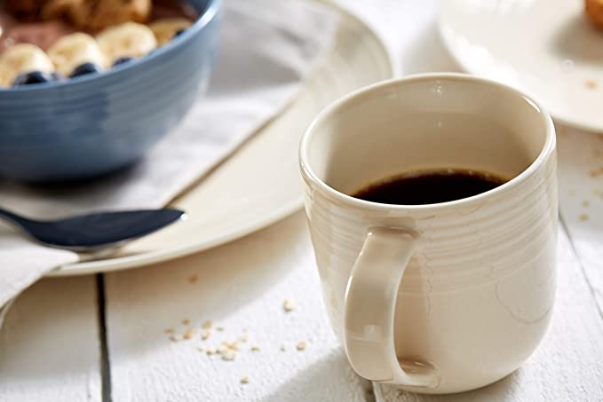 Geschirrset in Blau im Frühstücksambiente, mit beiger Tasse Beige Tasse mit schwarzem Kaffee auf hellem Holztisch, dahinter blauer Frühstücks-Bowl mit Banane und Heidelbeeren