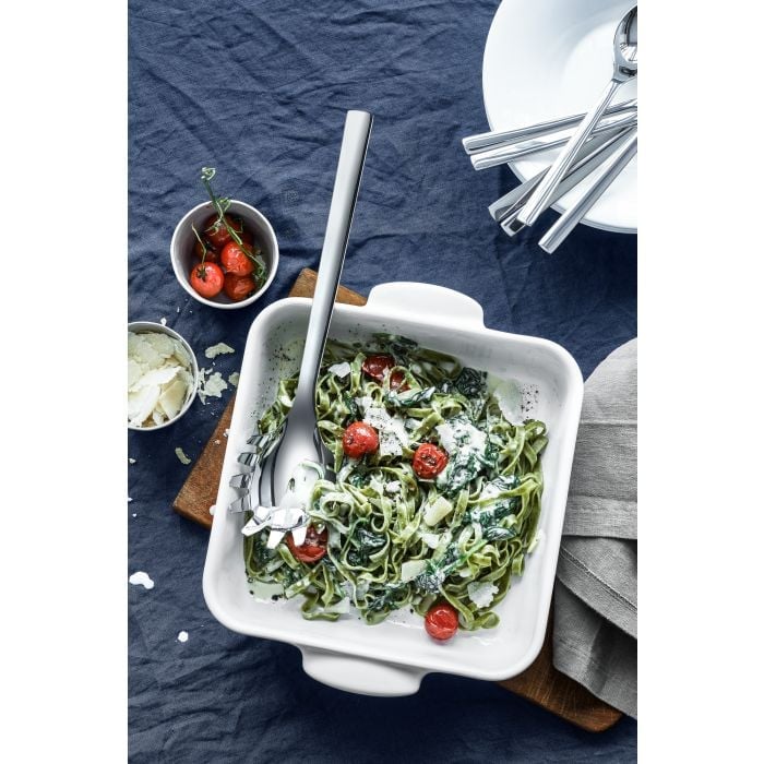 Obere Draufsicht auf weiße Schale mit grüner Pasta, Kirschtomaten, Soße und großem Besteck