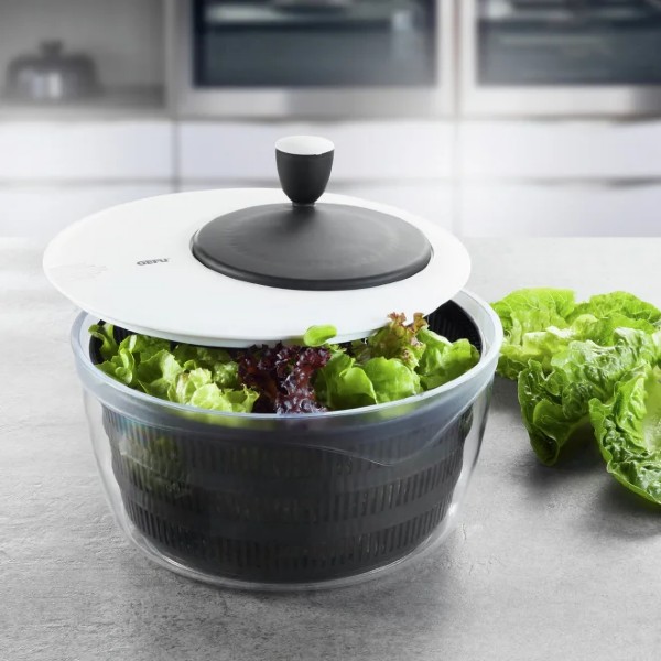 Von schräg oben: Salatschleuder mit schwarzem Deckel, gefüllt mit grünem und violettem Salat auf Küchenarbeitsplatte