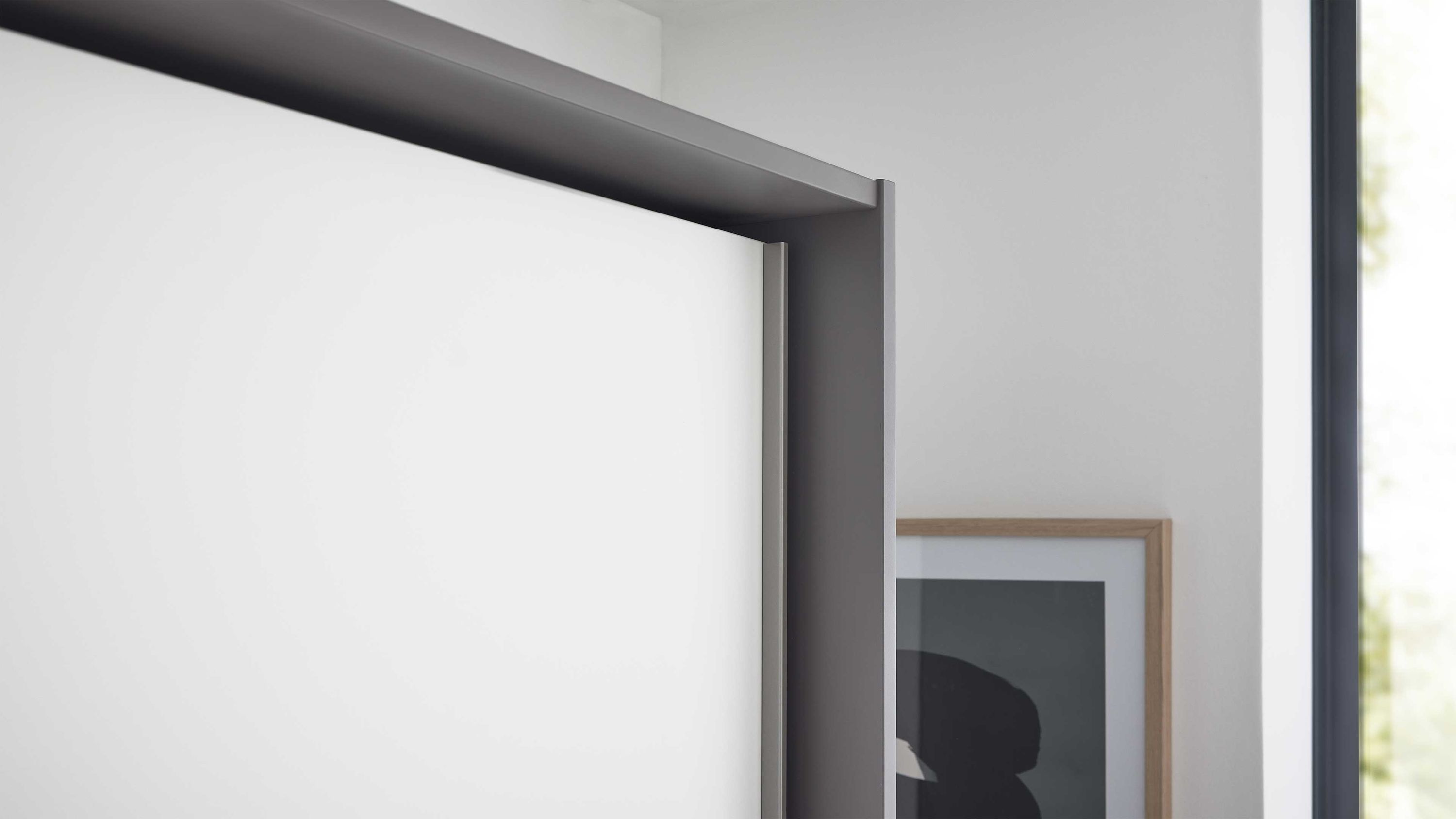 Eckansicht eines weißen Kleiderschranks mit grauem Rahmen und einem Bild an der Wand im Hintergrund