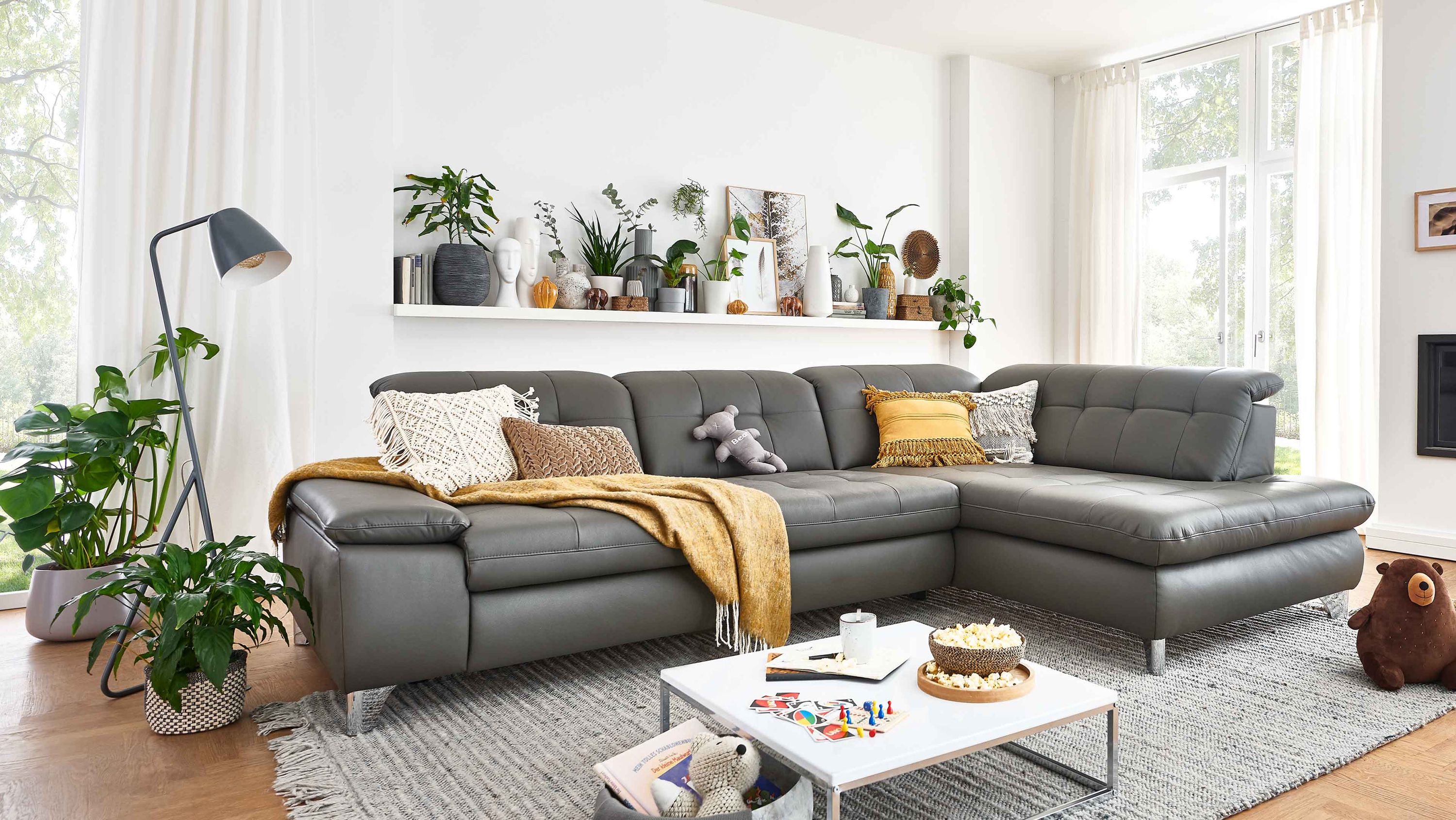 Ecksofa in grauem Leder mit glänzenden Winkelfüßen in modernem Wohnzimmer mit Pflanzen und Teppich