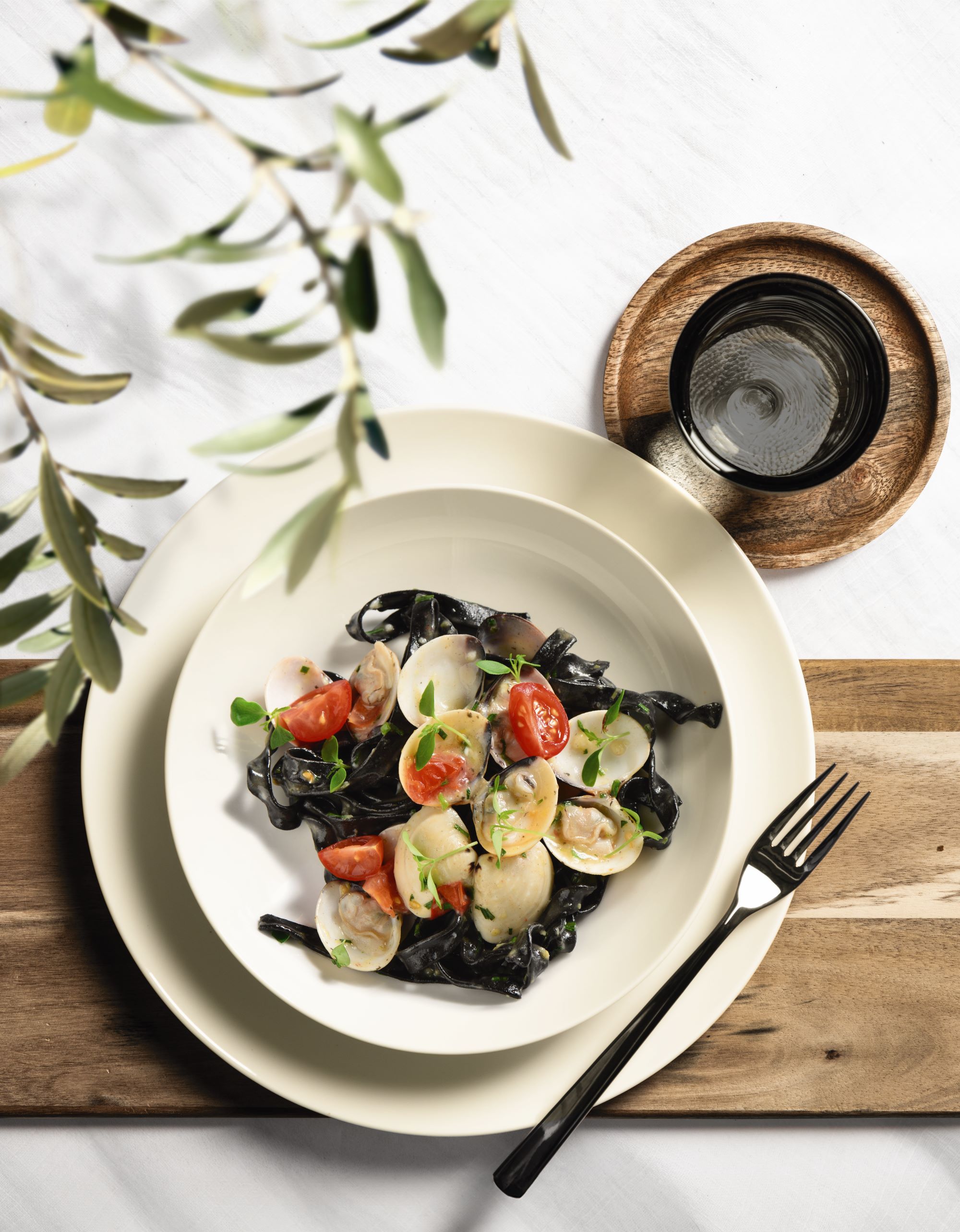 Rundes weißes Tafelservice mit flachem und tiefem Teller auf Holzbrett mit schwarzer Gabel und Glas auf Holzuntersetzer