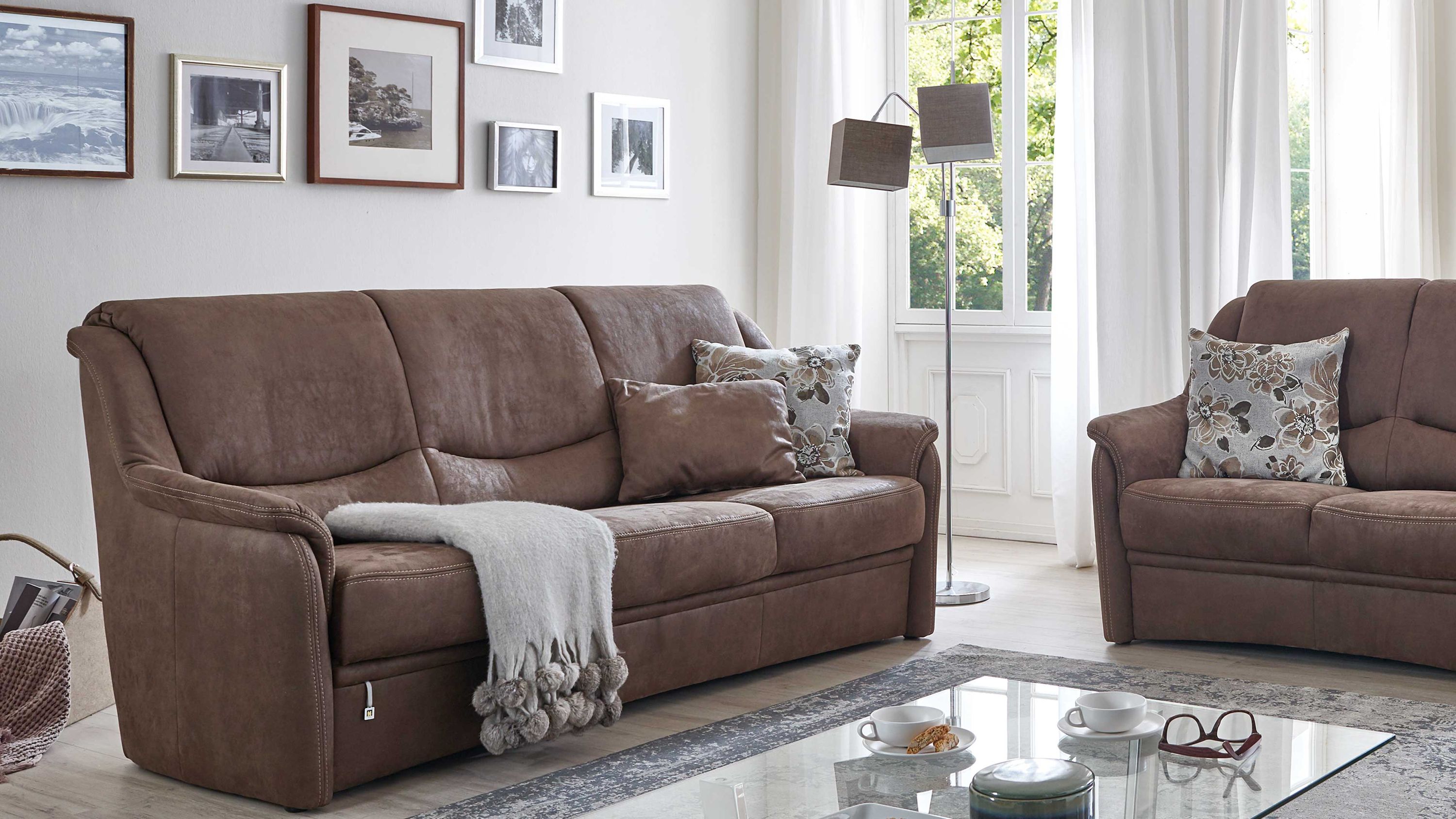 Dreisitziges Sofa in brauner Mikrofaser mit Kissen und Decke in einem hellen Wohnzimmer