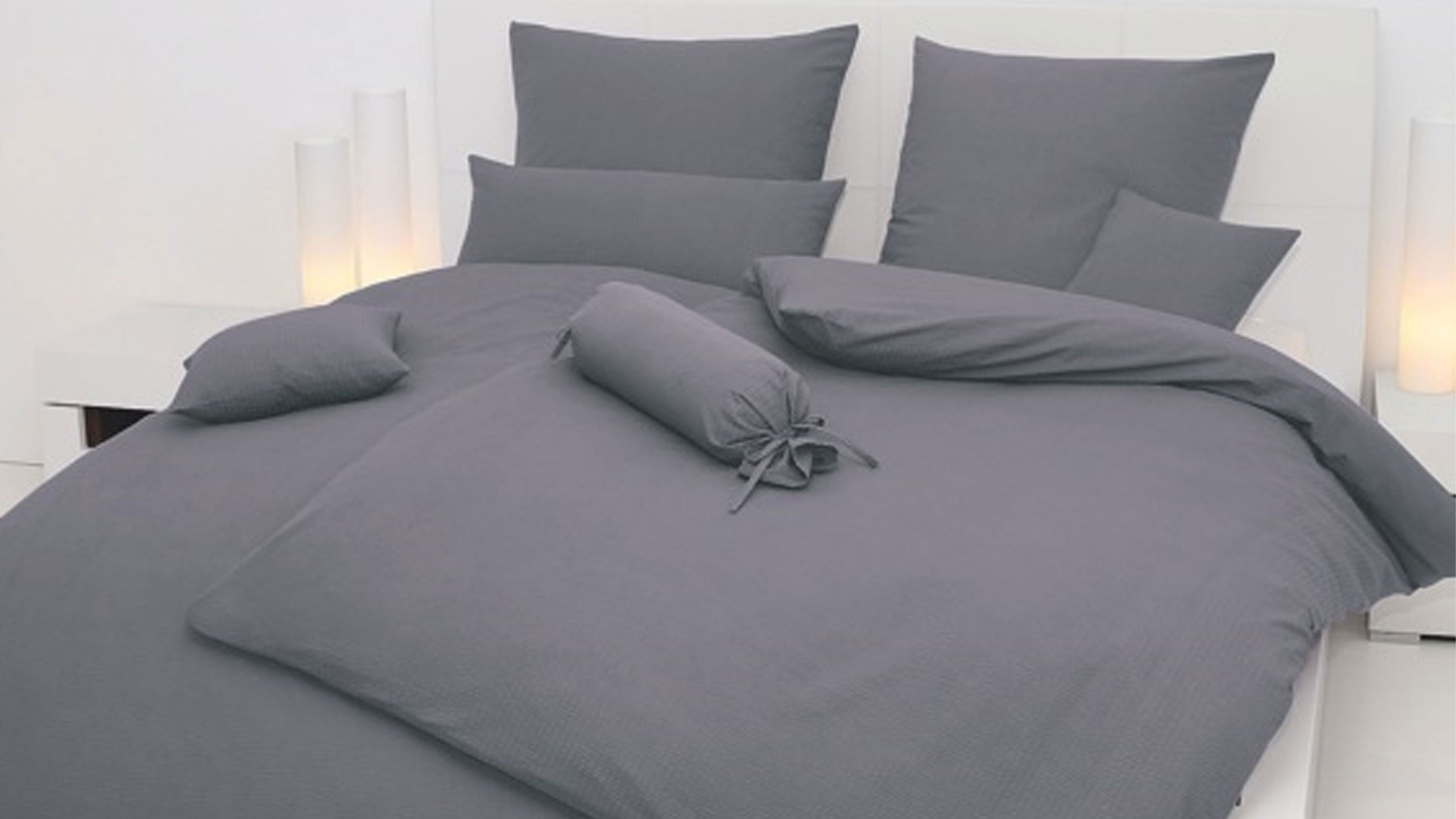 Grau melierte Bettwäsche mit Kissen und Zierrolle auf weißem Bett in hellem Schlafzimmer