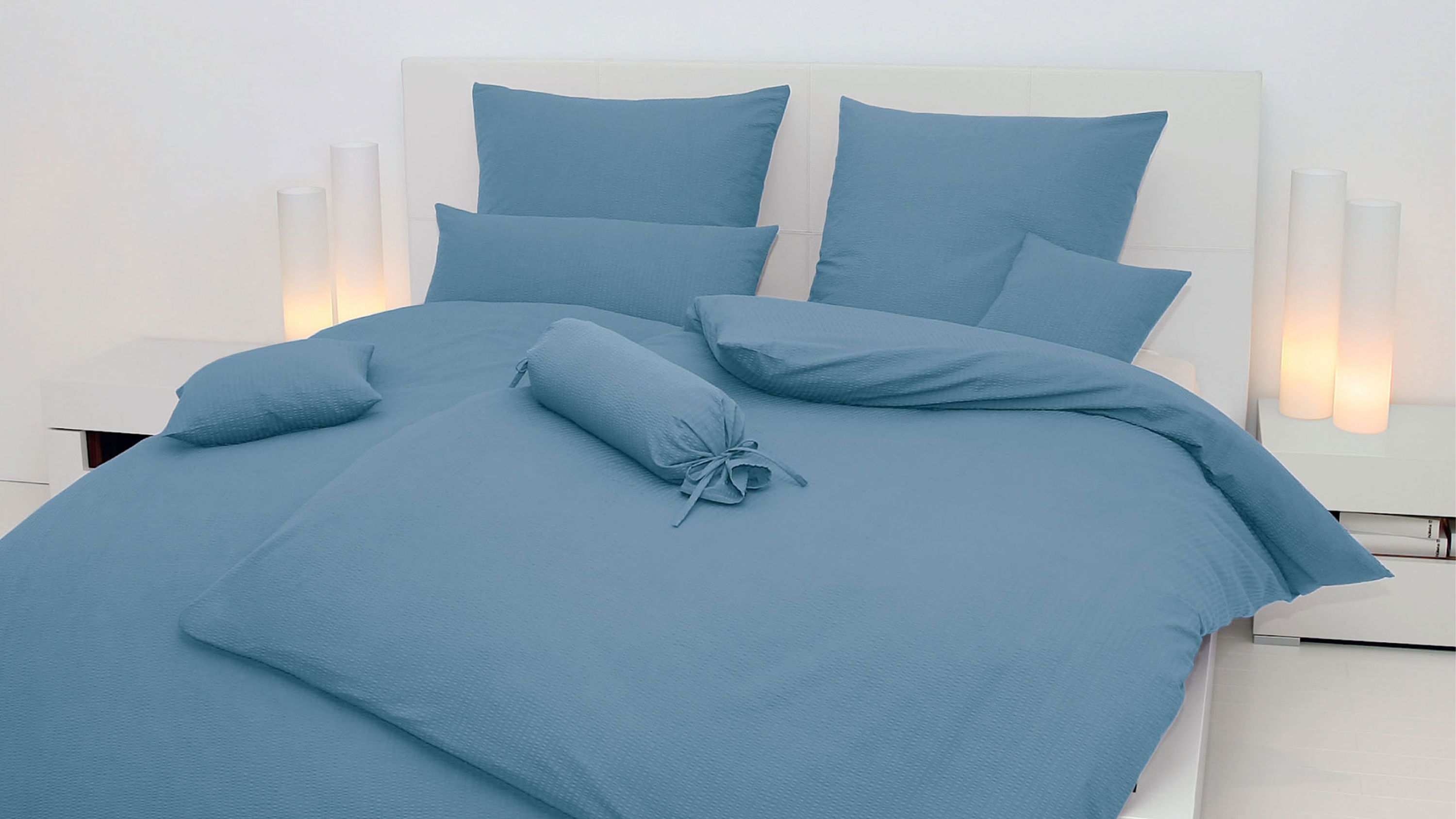 Bett mit hellblauer Bettwäsche bestehend aus Kissen Decke und Zierkissen in modernem Schlafzimmer