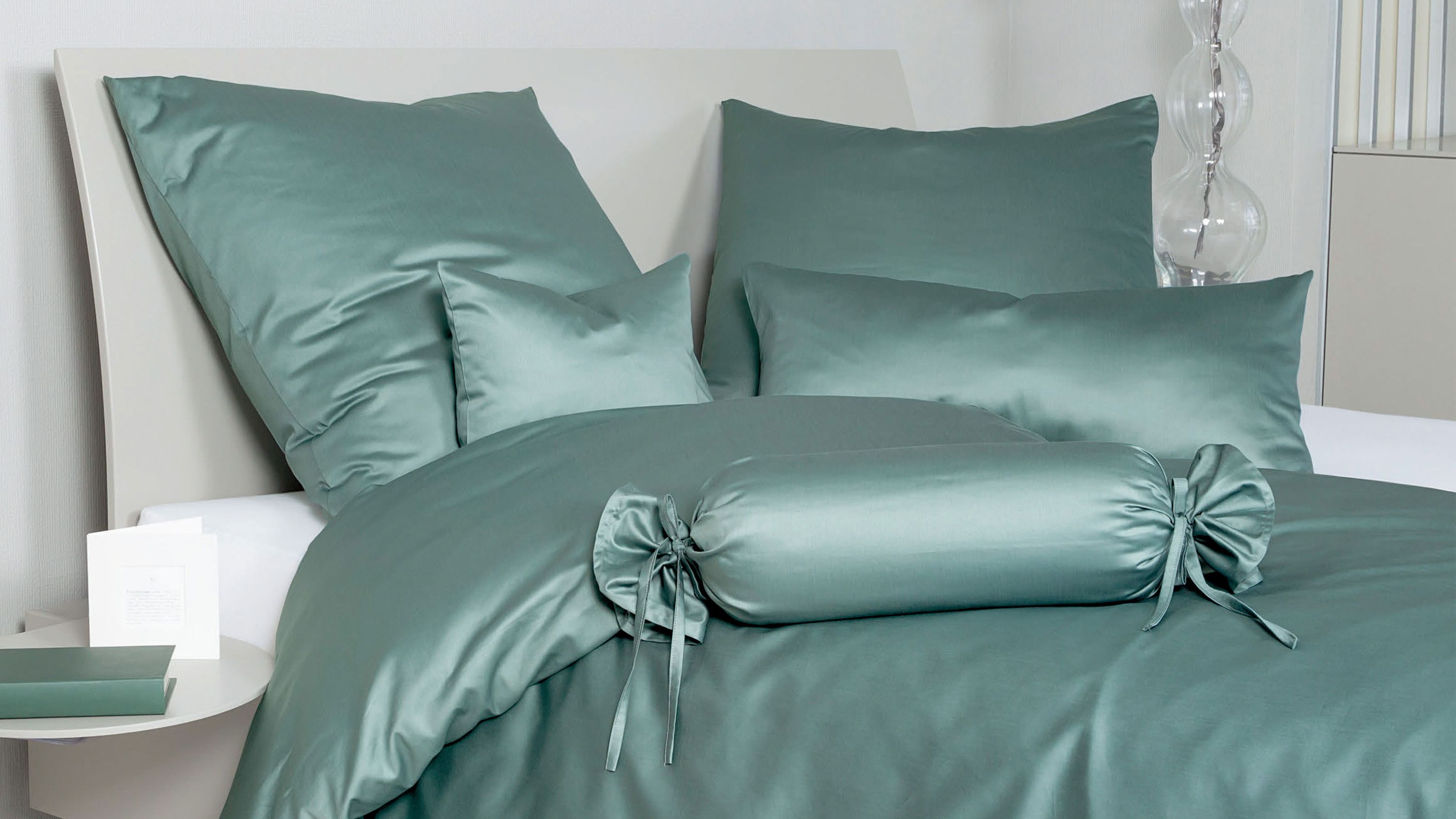 Bett mit glatter salbeigrüner Bettwäsche bestehend aus Kissen Decke und Zierrolle