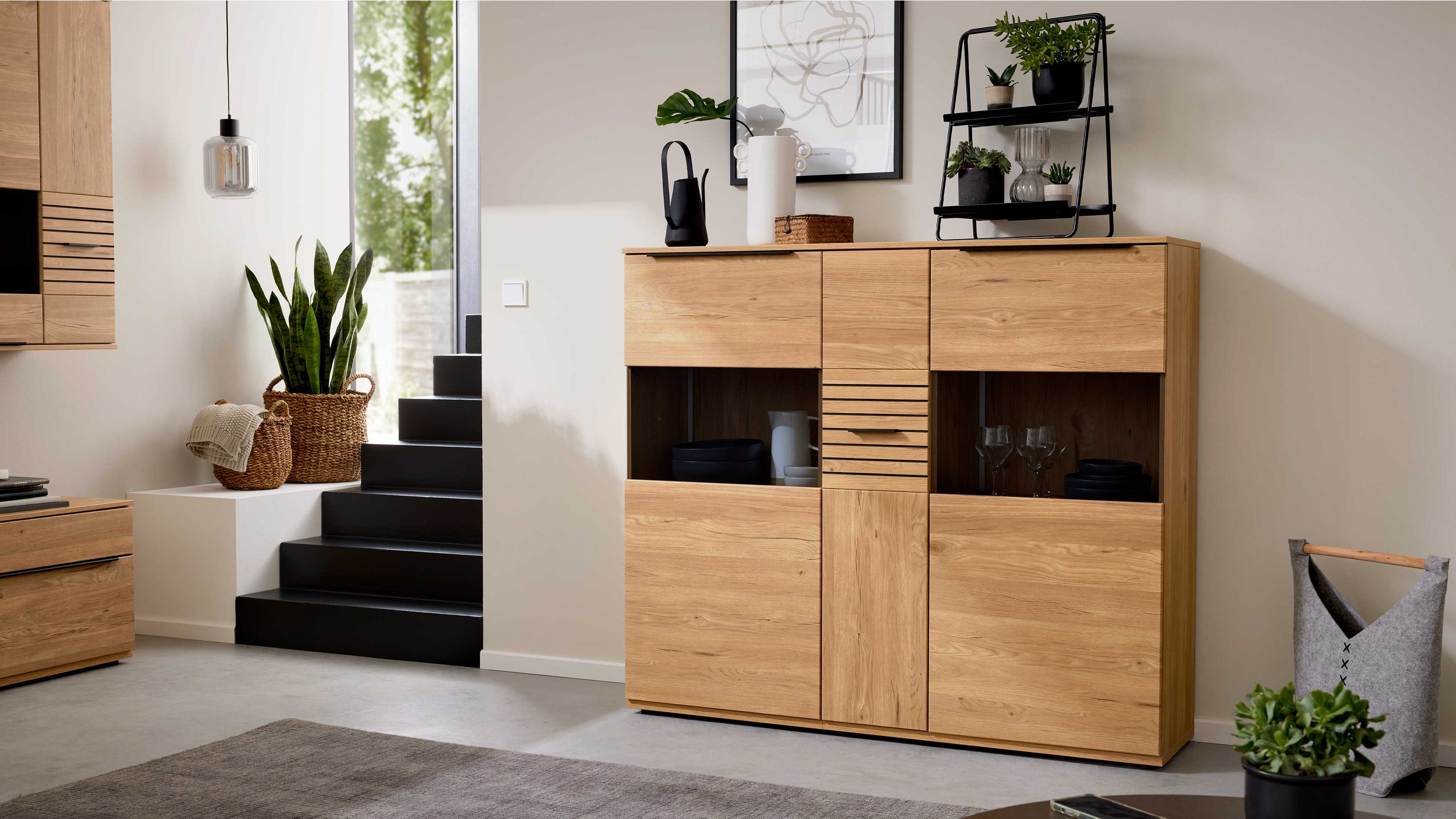 Highboard aus Holz mit zwei Türen drei Schubladen und offenen Fächern in einem Wohnzimmer