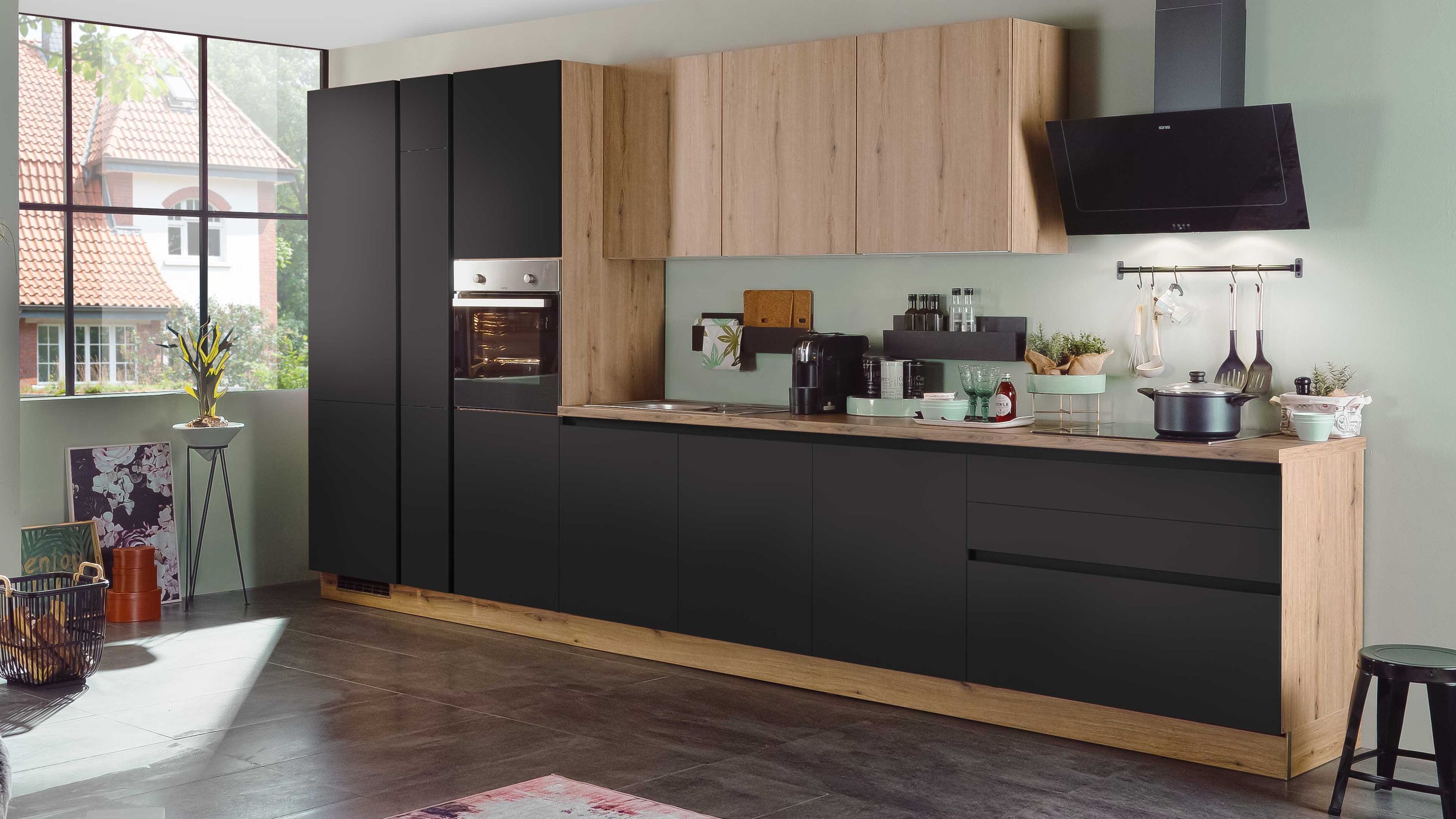 Moderne Küche in Schwarz-Holz-Optik mit Einbaugeräten heller Rückwand und großem Fenster.